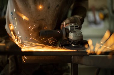 Öğütücüyle metal işleme. Aletten kıvılcımlar çıkıyor. Atölyede elinde öğütücüyle eldiven takan bir adam. Çelik gibi kıvılcımlar.