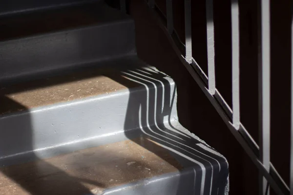 Stairs inside the house. Steps made of concrete. Details of the architect of the building. Gray steps and the shadow of the railing.