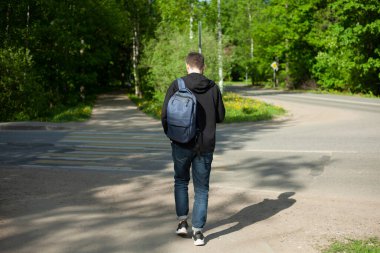 Sırt çantalı bir adam yol boyunca yürüyor. Yaya yolundaki adam mı? Arkadaki adam. Adam işe gidiyor..