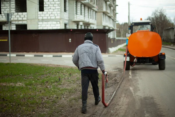 Bir işçi hortumla yolu yıkıyor. Bölgeyi temizliyorum. Asfalttan kir temizliyorum. Şehirdeki belediye hizmetleri.