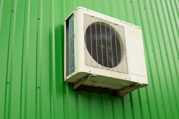 Air conditioning on the wall. Air conditioning outside the store. Green wall made of profiled sheet and white cooling device with fan. Industrial facility in detail.