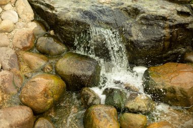 Taşların arasında şelale. Yapay gölet. Taşlar ve su ile peyzaj tasarımı. Büyük kaldırım taşlarının arasından akan su..