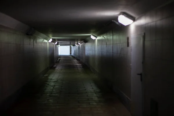 Tunnel under the road. Underground pedestrian crossing. A light in the end of a tunnel. Lamps in a long corridor.