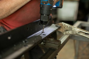 Bir adam metalde delikler açıyor. Adam garajda çalışıyor. Zor adam işi. Boşluk açarak..