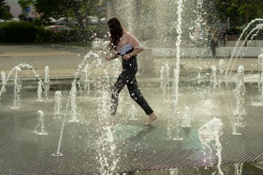 Kasaba meydanındaki su püskürtülerinin arasında bir çocuk koşuyor. Yazın fıskiyenin damlaları. Şehirde sıcak bir gün ve bir su kaynağı..