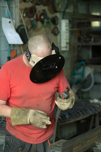 A masked welder works in a workshop. The man works with metal. The guy works in the workshop. Welding of steel seam.
