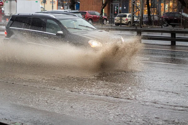 Araba bir su birikintisinde gidiyor. Tekerleklerin altından püskürtüyor. Su basmış bir otoyol. Işıkları yanan araç otoyola çıkıyor..
