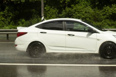 Araba ıslak bir yolda gidiyor. Yağmurdan sonra kaygan yol. Ulaşım tekerlerinin altından damlıyor. Otobana yağmur yağıyor. Banliyölerde yaz yağmuru.