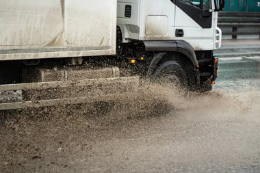 Araba bir su birikintisinin içinden geçiyor. Yoldaki su birikintisinden damlıyor. Sağanak yağıştan dolayı kirlenen araba otoyol boyunca sürüyor. Bir arabanın tekerleklerinin altında büyük bir su birikintisi.