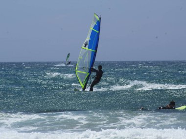 Bathers and sports enthusiasts on Guincho beach, in Cascais. June 30, 2021, Cascais, Portugal: Surfers, windsurfers and kite surfers enjoy winds and pleasant climate at Guincho beach, in district of Cascais, in metropolitan region of Lisbon