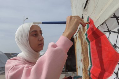 Gazze Limanı 'ndaki Yerdeğiştirme Kampları' nda Filistin Bayrağı Boyanmış. 8 Şubat 2026 Gazze, Filistin: Sanatçılar Farah Ajjour ve Şah Rajab, her ikisi de 20 'li yaşlarda, sıcak içecek satış büfesine Filistin bayrağının bir resmini yaptılar.