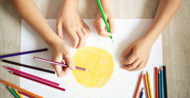 Çocuklar renkli kalemlerle bir resim çiziyor.