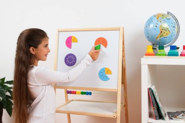 Matematik bölümleri ve tüm bölümleri öğrenmek için oyun bazlı yöntemler kullanan bir kızın eğitici çekimleri. Erken çocukluk bilişsel gelişiminde oyun ve çalışmanın birleşimini temsil eder..