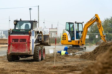 İnşaat alanında siper kazan iki küçük kazıcı. Siperlere boru döşeyen bir işçi. 