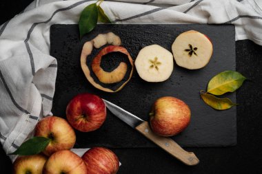 Elmalar siyah bir masada, bıçakla. Kesme tahtasının etrafındaki mutfak örtüsü. Parlak kırmızı ve sarı elmalar