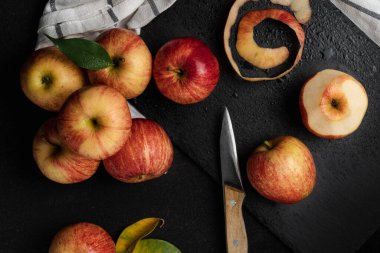 Elmalar siyah bir masada, bıçakla. Parlak kırmızı ve sarı elmalar kumaş üzerinde. 