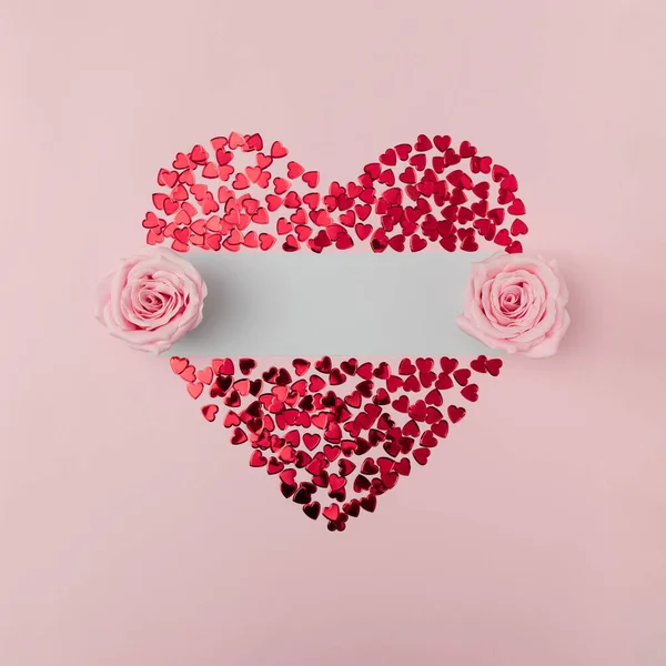 Big heart made of small red hearts with two pink rose flowers and copy space on bright pink background. St. Valentine, Mother\'s Day, birthday greeting cards, invitation, minimal celebrating concept.