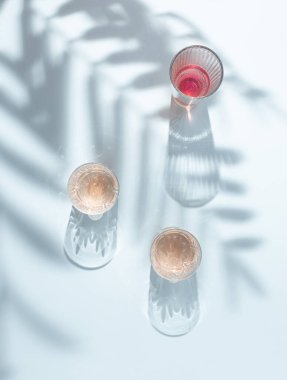 Yaz içkisi bardakları ve pastel mavi arka planda palmiye yaprakları. Yaratıcı asgari estetik. Düz yatıyordu.