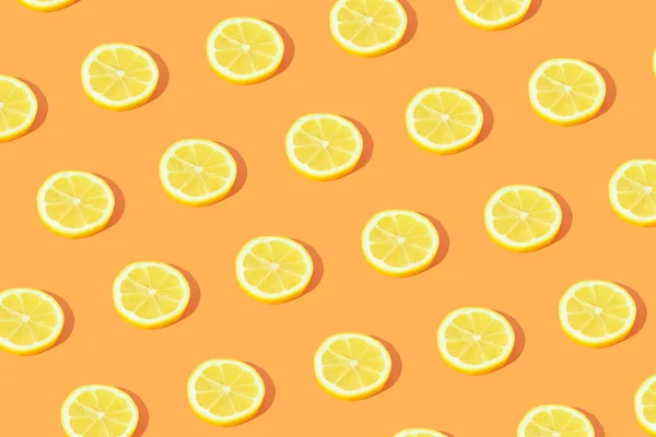 Minimal fruit pattern made with yellow lemon slices with sunlight shadow on bright orange background. Creative food concept.