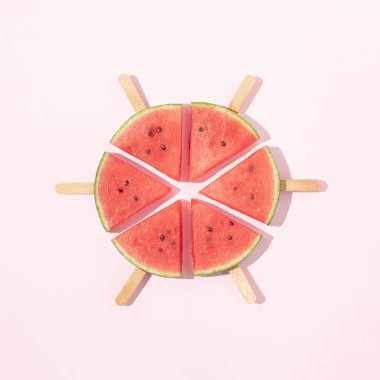 Pembe arka planda buzlu çubuklu taze karpuz parçaları. Minimum yaz meyvesi konsepti. Yaratıcı gıda düzenlemesi. Güneşli gün gölgeleri.