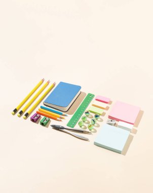 Yaratıcı bir şekilde düzenlenmiş okul malzemeleri, parlak bej arka planda güneş ışığı gölgeleri. Asgari çalışma alanı kavramı.