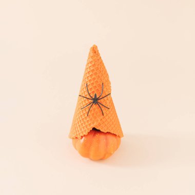 Turuncu balkabağı, dondurma külahı ve parlak bej arka planda siyah örümcek. Asgari Cadılar Bayramı konsepti Yaratıcı ürkütücü tatil partisi eğlence fikri.