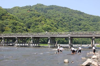 Çocuklar nehirde balık tutuyor. Japonya Oi Nehri 'nin karşısındaki Arashiyama Dağı.