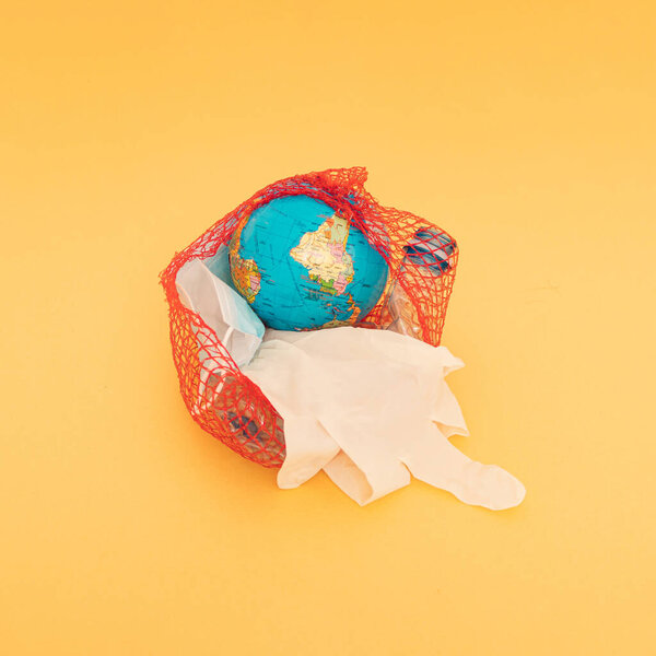 Globe, plastic bottle, blue surgical face mask and white glove in a nylon red bag. Golden background.