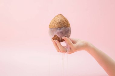 Güzel bir kadın eli, içinden salgı çıkan bir hindistan cevizi tutuyor. Pembe arkaplan.