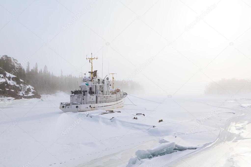 The ship which has frozen in in ice in a winter bay in the foggy