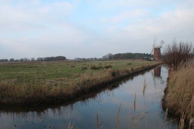 Eski tip yel değirmeni tuğla bina Horsey Pompası ahşap beyaz yelkenli günbatımı Norfolk Geniş su kanalı kırsal kırsal çiftlik arazisinde yansıyor.