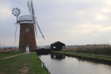 Eski tip yel değirmeni tuğlası bina Horsey Pompa ahşap beyaz yelkenler ve kulübe yansıyan günbatımı Norfolk Kanalı durgun su çiftlik arazisi soğuk yaz akşamında çevrili 