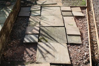 Bahçe inşaatının kapanışı. Kum taşı levhaları sert çimento ve çakıl üzerinde düz çizgiler halinde. İnşaat sırasında bahçe yolunda ahşap kenarlar ve sıcak bahar gününde tuğlalara yansıyan bitkiler.