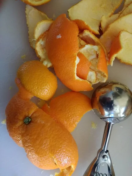 Close up of orange peel, the freshly peeled skin of the citrus fruit cut into thin strips for cooking home made vegan sweet dessert for lunch flat lay view on white kitchen cutting surface with metal ice cream scoop utensil for removing the sour pith