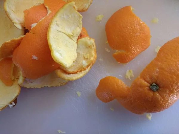 Close up of orange peel, the freshly peeled skin of the citrus fruit with yellow pith to be removed being prepared to make vegan sweet dessert for lunch flat lay view  on white kitchen surface