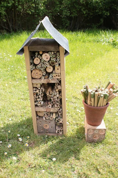 Close up of bee hotel, a recycled wood, branches and bamboo construction for the conservation of bees giving nest space  and protection in the garden sat on grass lawn with earthenware pot of pre cut bamboo sticks with natural holes for nesting