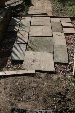 Bahçe inşaatının kapanışı. Kum taşı levhaları sert çimento ve çakıl üzerinde düz çizgiler halinde. İnşaat sırasında bahçe yolu için ahşap kenarlı.