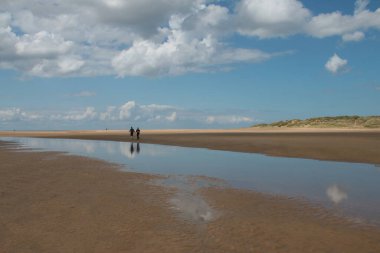 Holkham Norfolk 'un güzel manzarası deniz kıyısında tatilde olan bir çiftin deniz suyu göllerinde yansıyan beyaz, kabaran bulutlarla alçak gelgit yaz mavi gökyüzü.