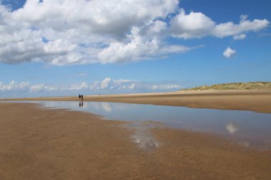 Holkham Norfolk 'un güzel manzarası deniz kıyısında tatilde olan bir çiftin deniz suyu göllerinde yansıyan beyaz, kabaran bulutlarla alçak gelgit yaz mavi gökyüzü.
