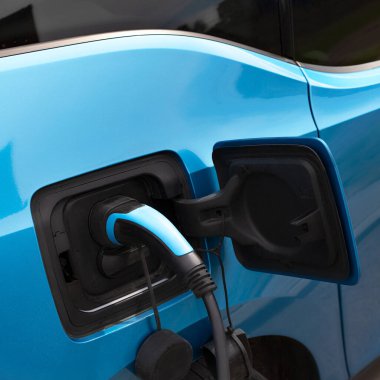 Elektrikli araba şarj oluyor. Arabaya bağlı olan şarj cihazının yakın çekimi. Mavi adaptör, mavi araba..