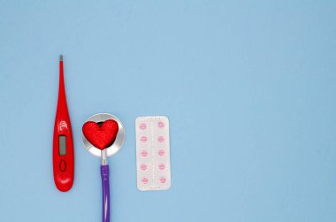 Stetoskop, termometre, kırmızı kalp ve kırmızı haplar kabarıklıklarda mavi arka planda fotokopi alanı ile birlikte. Tıbbî açıdan. Kardiyoloji. Sevgililer Günü Konsepti.