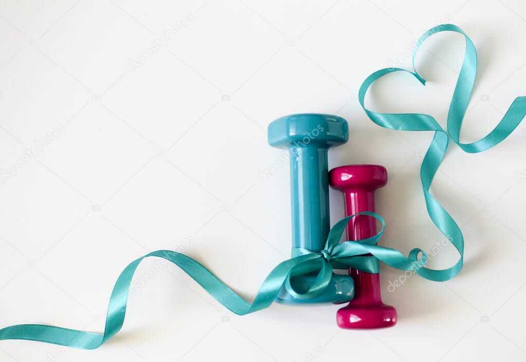 Two turquoise and pink dumbbells with ribbon bow on white background with copy space. Concept Valentines day, male and female, healthy lifestyle, giving gifts, love of sports. Trendy color green tide.