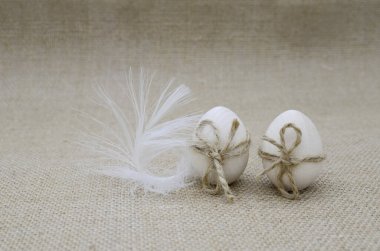 İp yaylı iki ahşap yumurta ve çuval bezinde beyaz kuş tüyü. Paskalya, doğum kavramı.