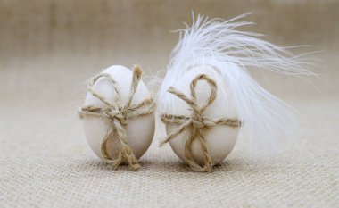 İp yaylı iki ahşap yumurta ve çuval bezinde beyaz kuş tüyü. Paskalya, doğum kavramı.