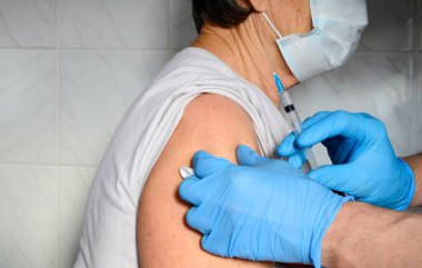 Tıbbi maskeli yaşlı kadın hastanede aşı yaptırıyor. Mavi eldivenli eller kadının ön koluna aşı enjekte ediyor. Aşı kavramı, Coronavirus Covid19.