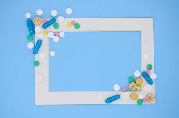 White frame and a lot of colorful medical pills, capsules on blue background with copy space.