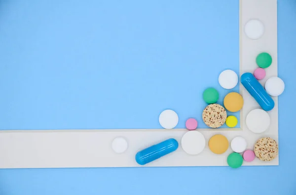 White frame and a lot of colorful medical pills, capsules on blue background with copy space.