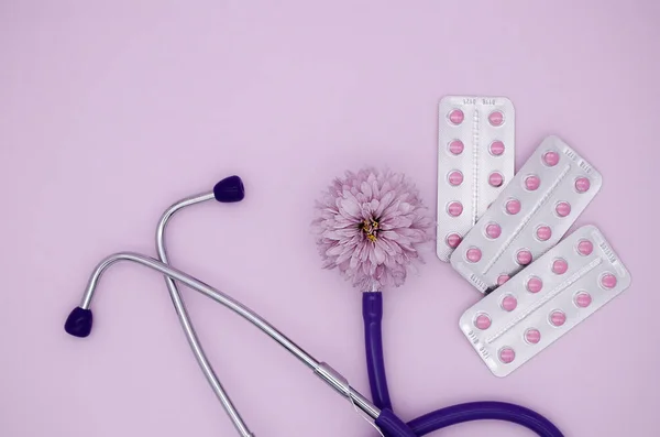 Stethoscope, three blisters with pink medical pills on pink background with copy space. Medical flat lay.