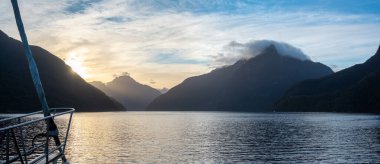 Kuşkulu Ses 'in üzerinde yükselen güneş Yeni Zelanda' nın Güney Adası 'ndaki dağlarda sarkan bulutlar.