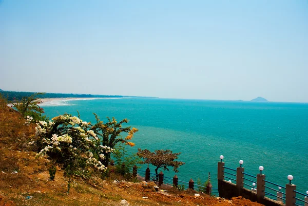 Pohled na moře. Zelené keře s bílými a červenými květy. Murudeshwar. Karnataka, Indie. — Stock fotografie